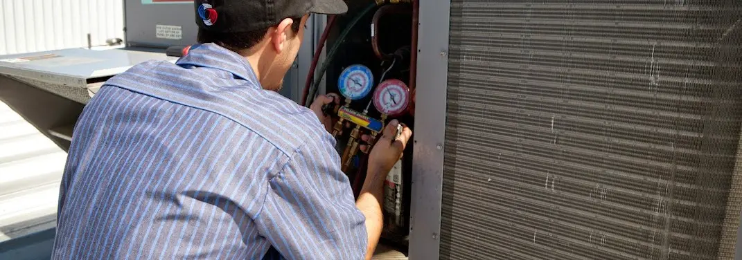 HVAC technician servicing a condenser unit in Turner
